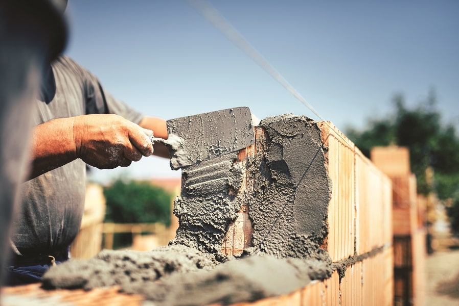 A construction worker applying cement on bricks with a trowel during the construction of a wall.